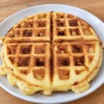 Basic keto chaffles, golden and crispy, cut into four sections on a white plate