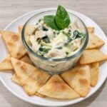 Keto spinach artichoke dip with chicken in a glass bowl, surrounded by golden, crispy tortilla chips.