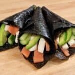 Three salmon hand rolls wrapped in nori and filled with smoked salmon, cream cheese, avocado, and cucumber.