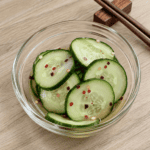 Thinly sliced English cucumbers in a glass bowl with tangy dressing and red pepper flakes, prepared as a keto sunomono cucumber salad.